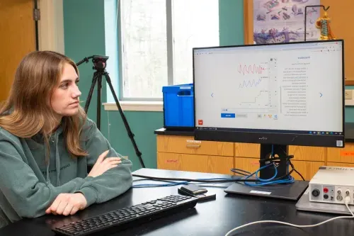 A student looks at a line graph with a red line, blue line, and green line on a monitor