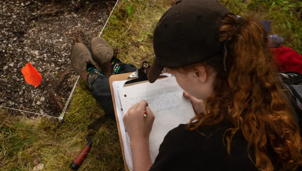 A student sitting on grass is writing notes