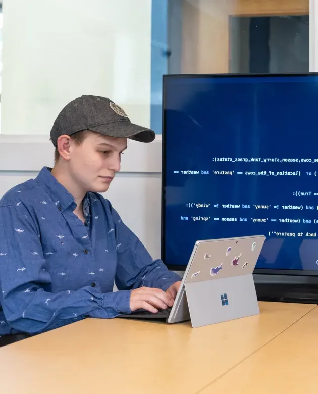 A student works on a coding project on their iPad as it shows behind them on a large monitor